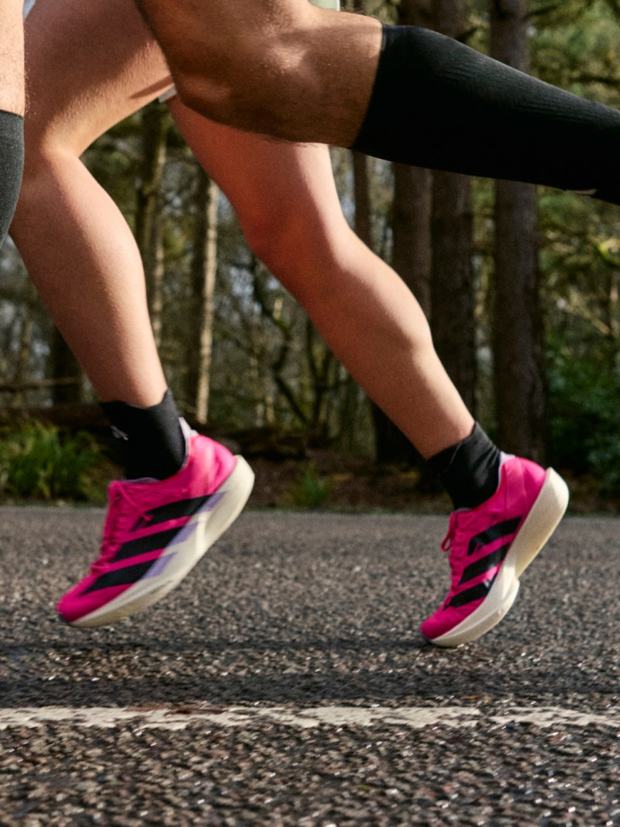 A runner wearing pink adidas Adizero Boston shoes on a woodland road