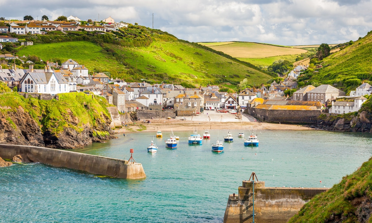 Boats in a Cornish harbour beneath green hills and village cottages